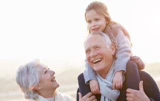 Großeltern lachen mit Enkelin auf den Schultern des Opas am Strand | Immobilienverrentung