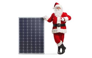 Ein Weihnachtsmann lehtn an einer Photovoltaikanlage - Weihnachtsgrüße