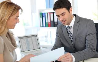 Mann und Frau sitzen am Schreibtisch mit Papier und Laptop - Immobilienkredit