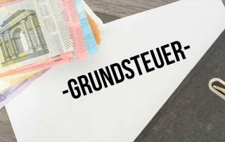Auf einem Schreibtisch liegen Geldscheine, ein Ordner und ein Papier mit dem Wort "Grundsteuer" - Grundsteuer
