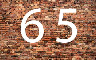 Die Zahl 65 in weiß vor einer Backsteinwand - Rohstoff Holz