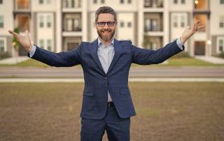 Ein Verwalter in witziger Pose vor einem Mehrfamilienhaus