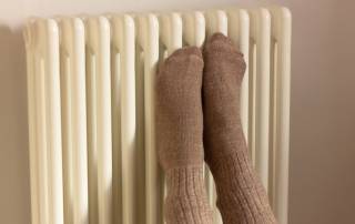 Jemand presst vor Kälte seine Füße mit Socken an eine Heizung, um nicht zu frieren